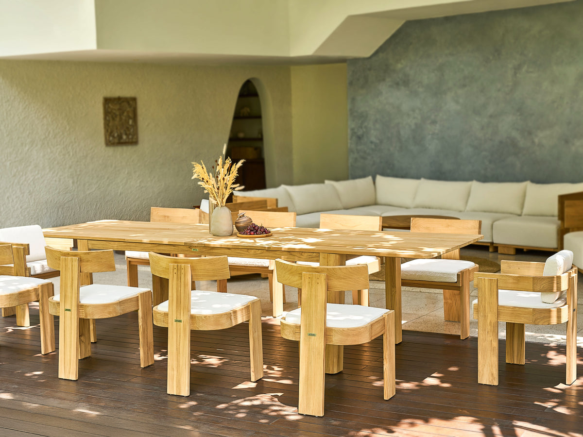 FORMA DINING TABLE set in a bright outdoor patio featuring natural teak wood with cushioned seats, surrounded by a cozy white sectional sofa and minimalist decor.