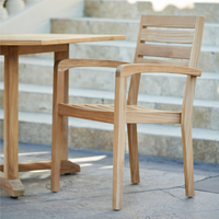 An outdoor dining setup with teak furniture on a wooden patio, surrounded by lush greenery, creating a serene and inviting atmosphere.