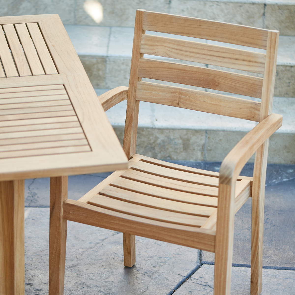 A close-up of the teak armchair and table, highlighting the natural wood's texture and durability in a bright outdoor setting.