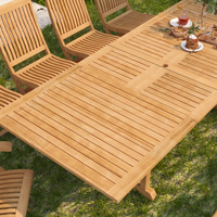 A close-up of the teak dining table's slatted surface, beautifully set for an outdoor brunch, highlighting the natural wood grain and craftsmanship in a lush garden setting.