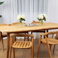 A seven-piece dining set featuring a rectangular teak wood table with a live edge and six matching armchairs, placed on a wooden floor against a white backdrop. The table is set with drinks and decorative items, showcasing its use and the aesthetic appeal of the La Costa Collection.