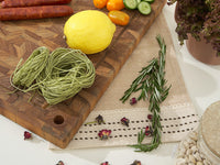 Wooden Teak cutting board with green pasta, lemon, and vegetables on a table.